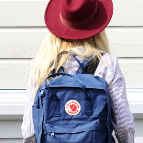 En ungdom med röd hatt och ryggsäck som står bortvänd från kameran